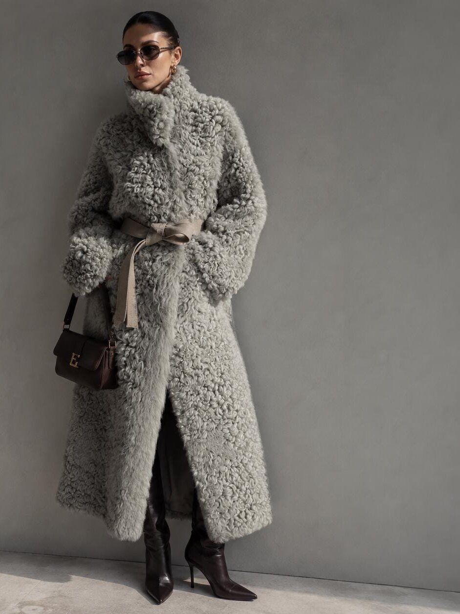 Grey floor-length reversible Spanish lambskin tigrado fur coat, belted, against a grey wall